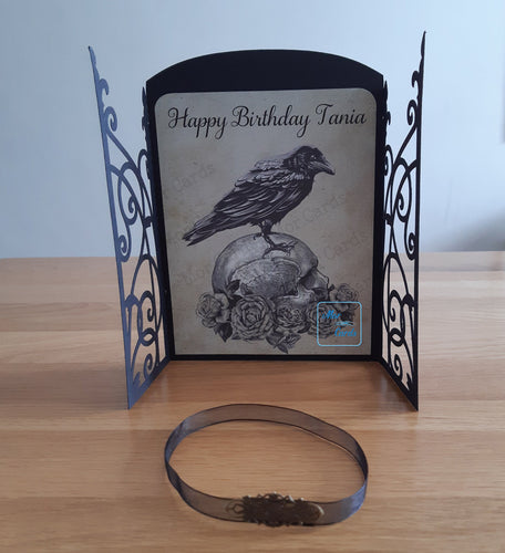 Gatefold style card with a crow stood on a skull resting on roses